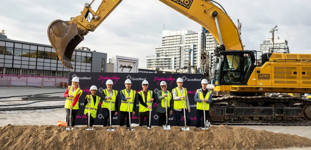 A group of people in safety vests and helmets standing at a construction site with shovels.