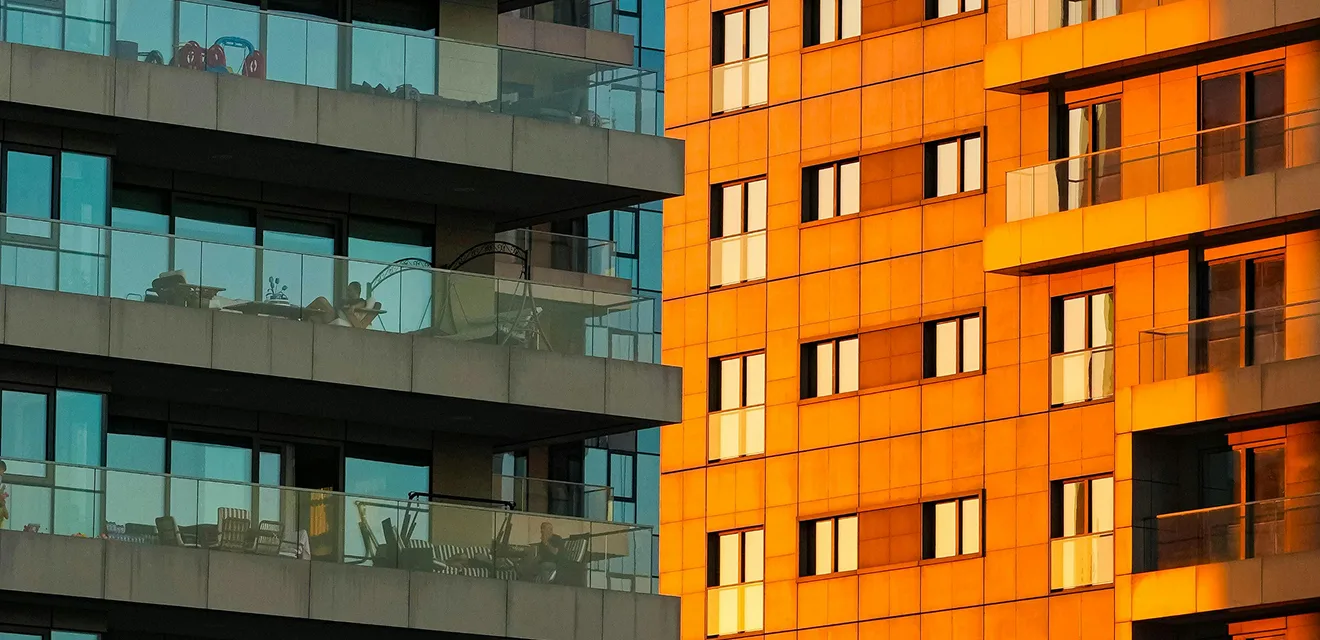Close-up of two modern apartment buildings with balconies. One building is reflecting the warm light of the sunset.