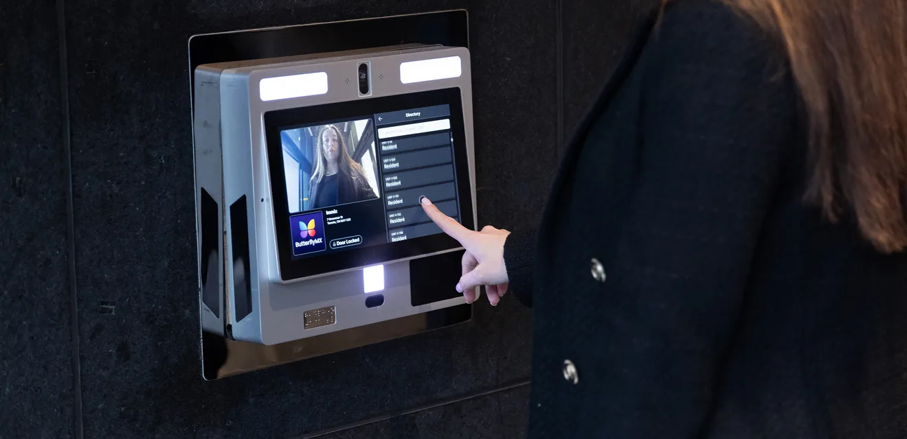 A person is using a touchscreen security or intercom system mounted on a wall, interacting with its digital interface.