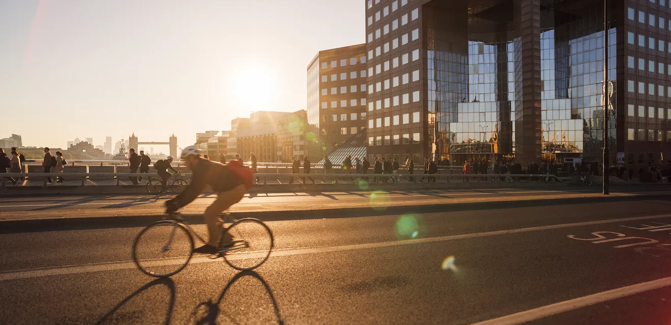 A cyclist riding on a sunlit street with modern buildings in the background.