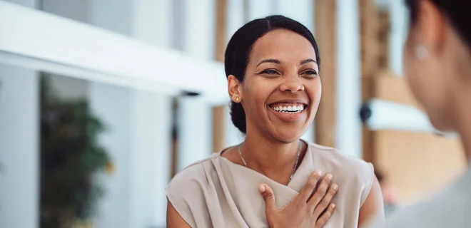 A person with her hand over her heart smiling in conversation.