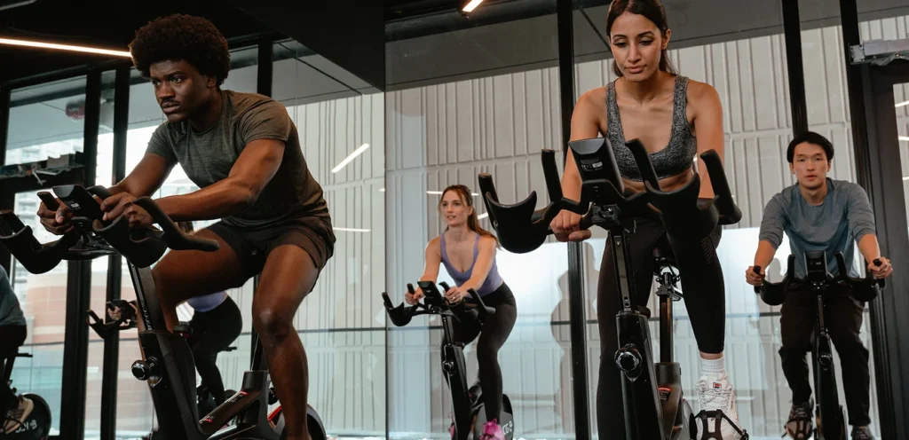 A group of people are engaged in a spin class, intensely focused on stationary bikes in a modern gym setting.