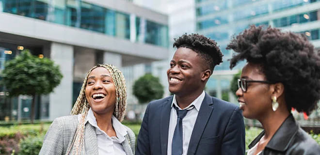 Three professionals are standing outside a modern office building, smiling and engaged in conversation. The atmosphere is lively and positive.