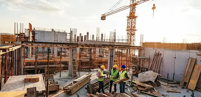 Construction site with workers in safety vests and a crane in the background.
