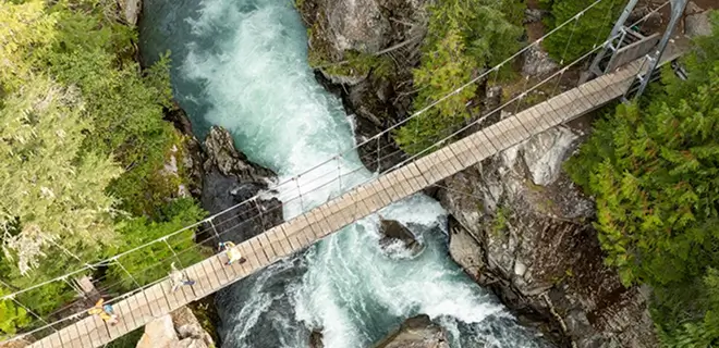 Aerial view of a suspension bridge over a river in a forested area.