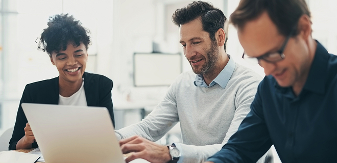 L’image montre trois personnes assises à une table, engagées dans un travail.