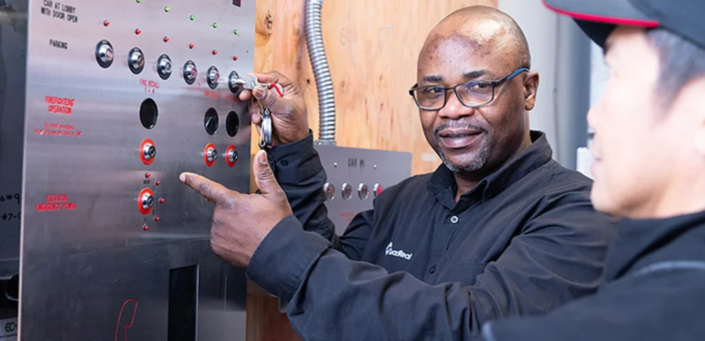 Deux techniciens discutent et examinent un panneau de commande avec divers boutons et indicateurs dans un environnement professionnel.