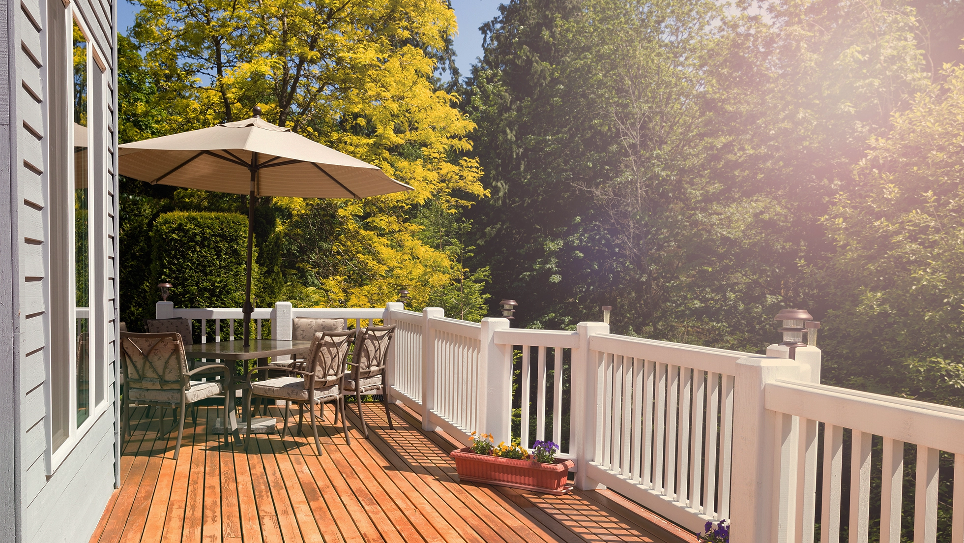 A wooden deck with a patio umbrella and chairs surrounded by trees.