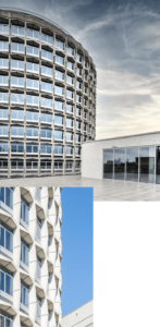 A modern, circular building with a grid-like glass facade set against a cloudy sky. The structure's design is sleek and contemporary, with an expansive open area in the foreground.