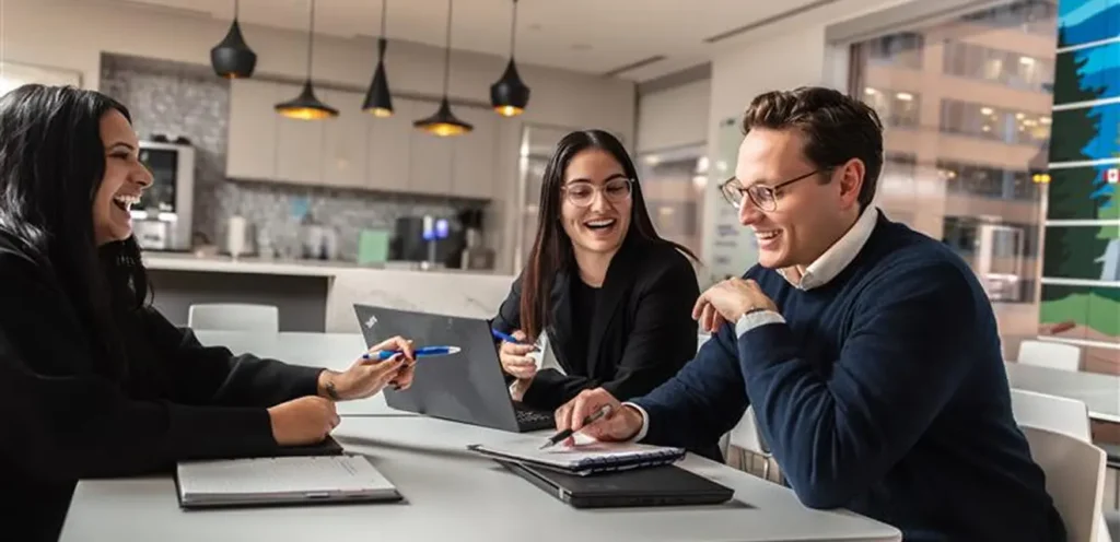 A group of laughing coworkers reviewing notes in a room.