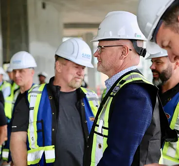 A group of people in construction hats and safety vests standing at a construction site.