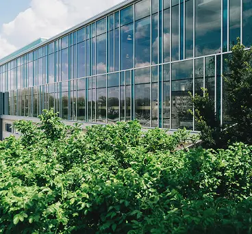A sleek glass walled building with greenery outside.