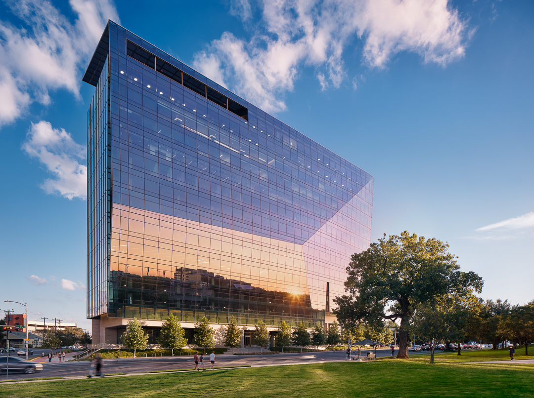 A modern glass office building with a tree in the foreground.