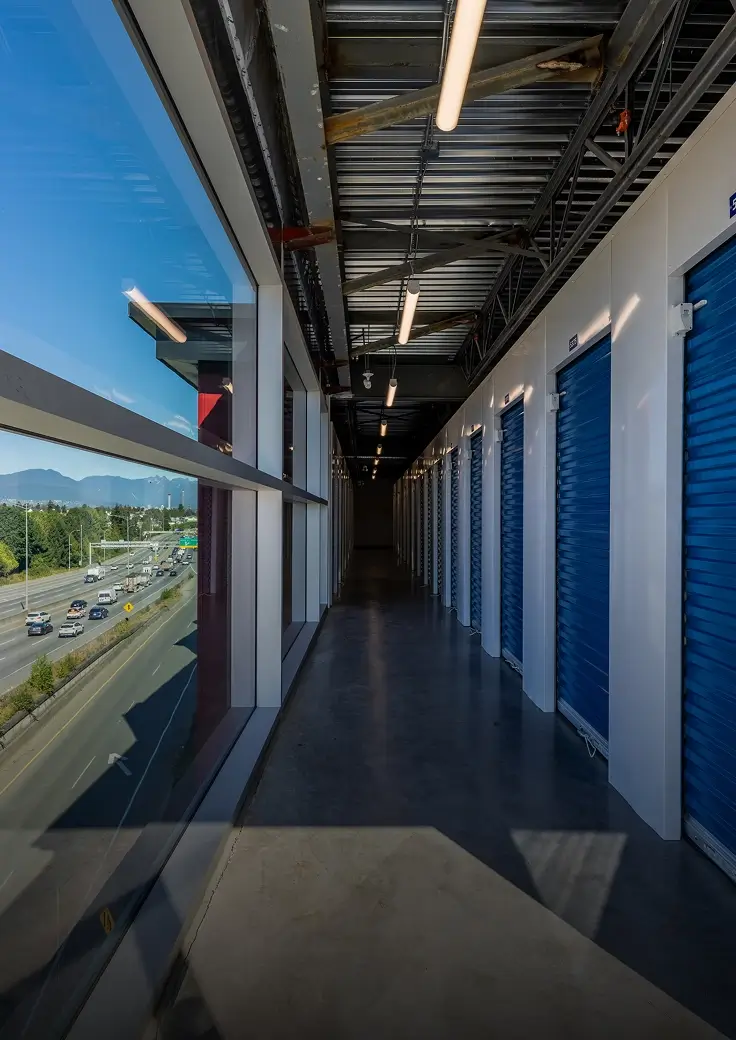 A hallway interior with glass windows on the left and blue doored storage units on the right.