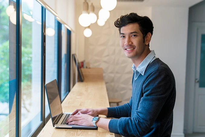 L’image montre une personne assise à un comptoir élevé qui travaille sur un ordinateur portable. 
