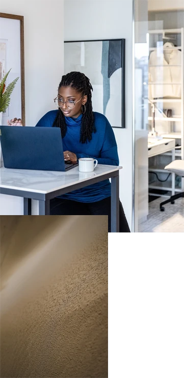 1. A person in a blue sweater working at a marble desk on a laptop with abstract art on the wall behind. 2. An abstract image of sand coming into focus.