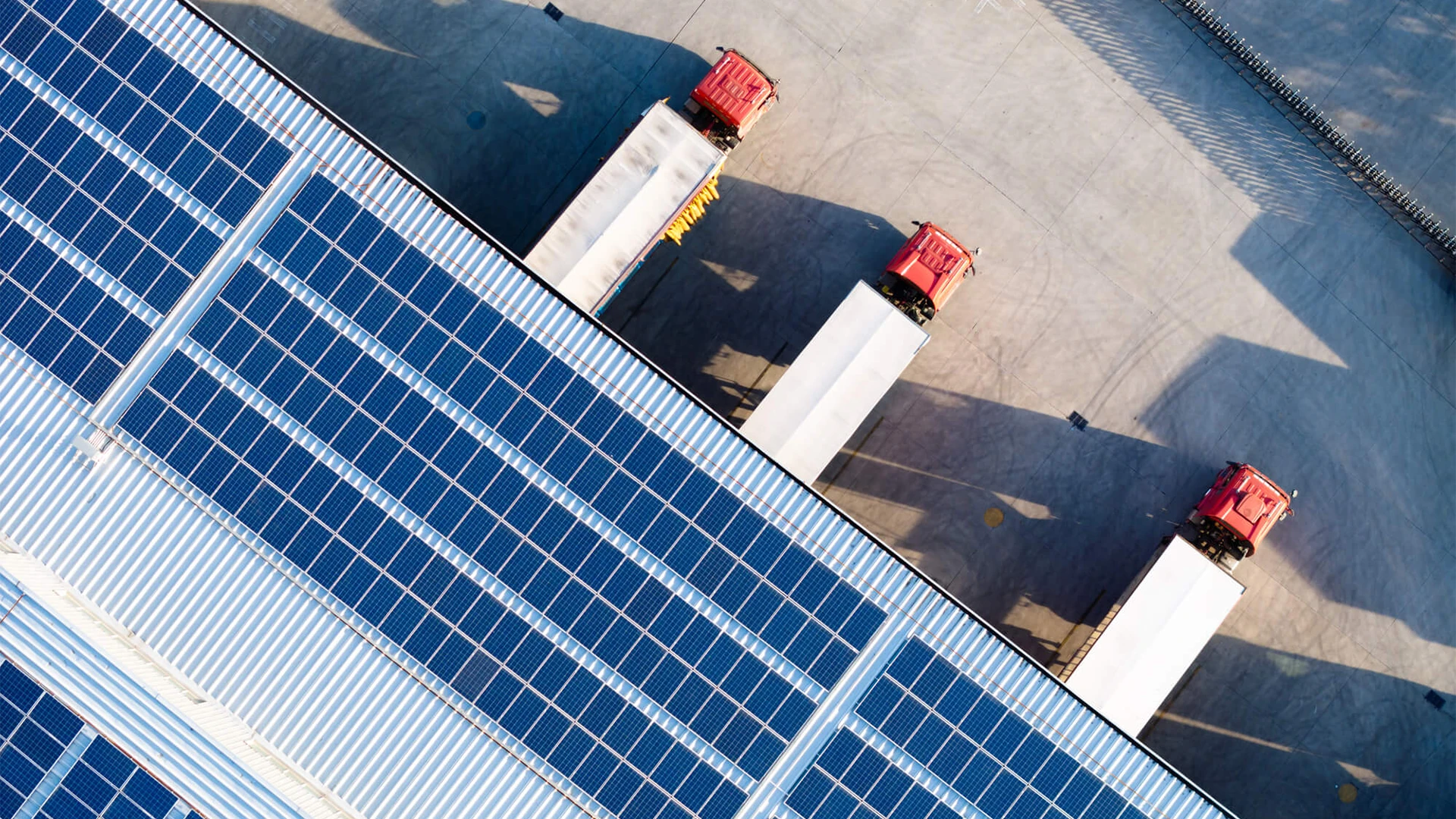 Aerial view of a solar-panel-covered warehouse roof with red trucks at loading docks.