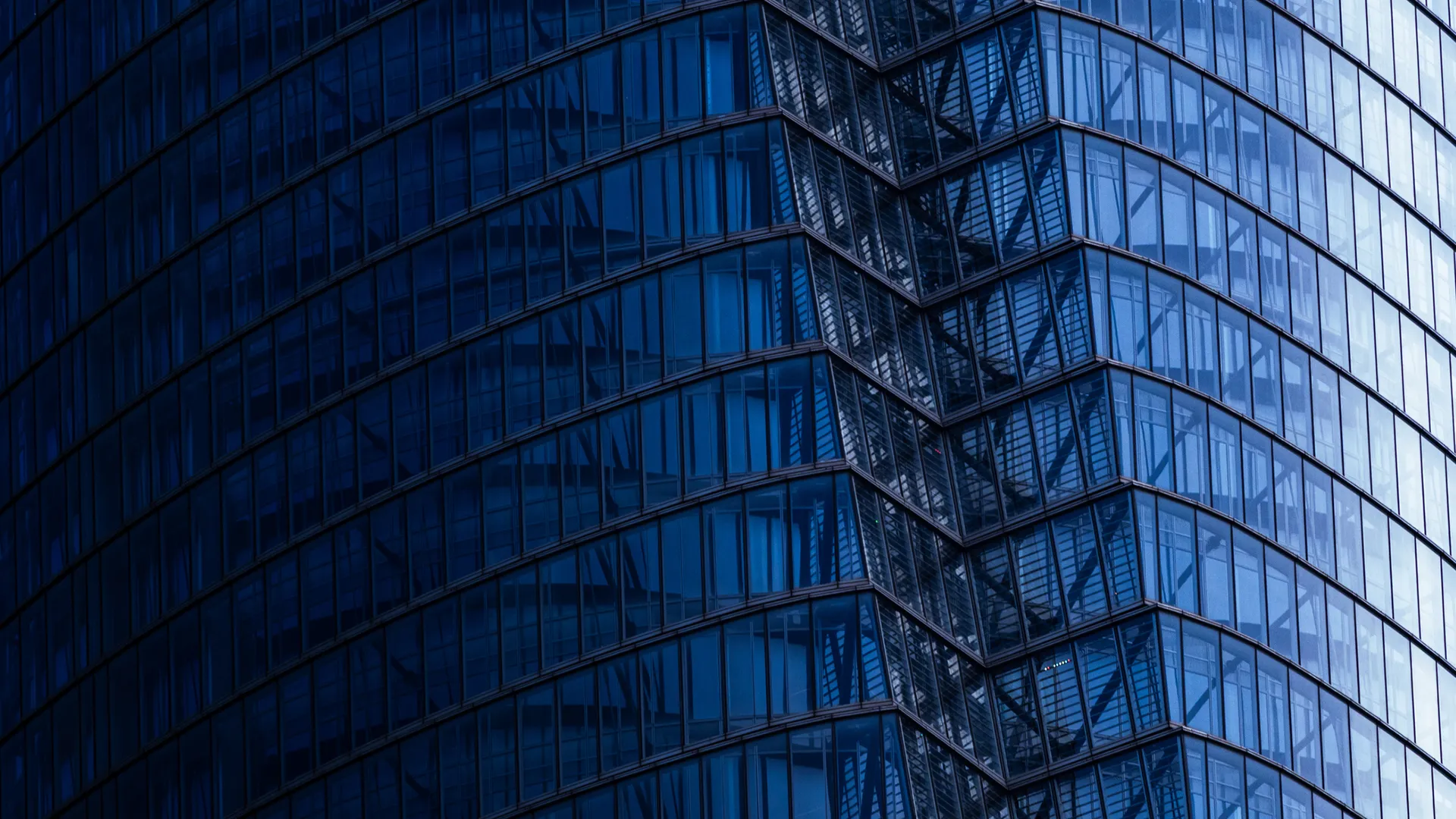 Close-up view of a modern glass skyscraper façade with repeating blue-tinted windows and diagonal architectural lines creating a geometric pattern.