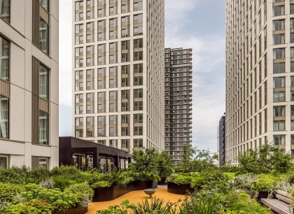 A view of a modern apartment complex with tall buildings and a landscaped courtyard featuring greenery.