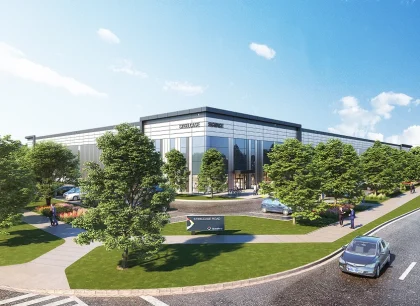 A modern, sleek building surrounded by a circular driveway and landscaped greenery, with cars parked alongside. The sky is bright and clear.