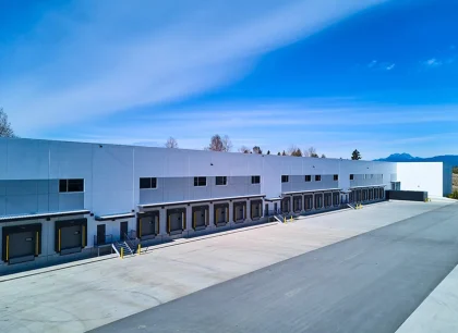 A large industrial warehouse with loading docks, set against a clear blue sky. The area is spacious and well-maintained.