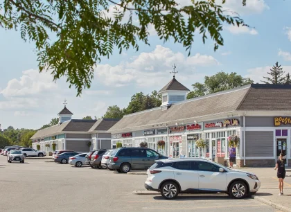 On the left, a traditional shopping center with a row of stores, parked cars, and a clear sky.