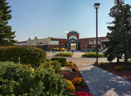 A traditional shopping center with a landscaped entrance, featuring a pathway and a clear blue sky.